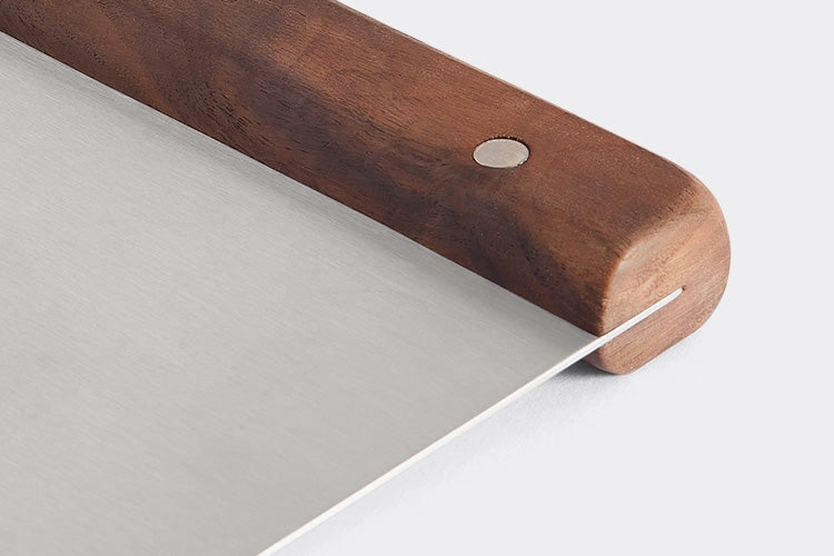 A close-up view of the Misen Bench Scraper’s walnut handle, on a white background, with part of the metal blade visible.