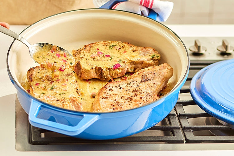 A blue Misen Enameled Cast Iron Braiser searing three large steaks with plenty of space between them on a stovetop.