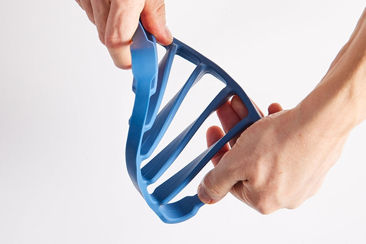Two hands hold a blue Misen Silicone Roasting Rack at each and and twist, showing the flexible bend of the rack.