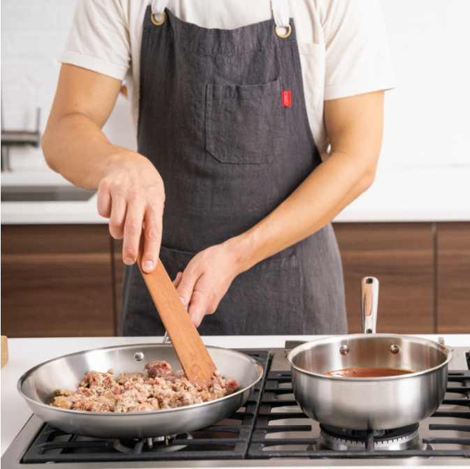 Browning ground beef in a Misen stainless steel pan next to a Misen saucier with tomato sauce and a Misen stockpot boiling spaghetti noodles