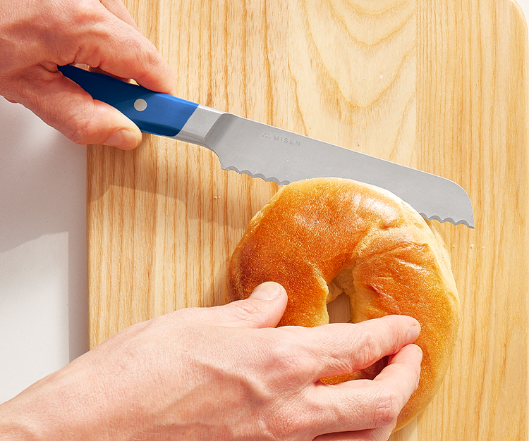 Using a short 6.5 inch blue serrated knife to cut a bagel in half.