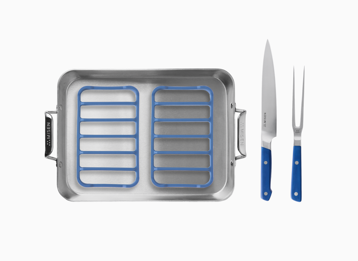 A Misen 13 inch Roasting Pan with two blue Misen Silicone Roasting Racks, accompanied by a Misen carving knife and a carving fork, both with blue handles. 