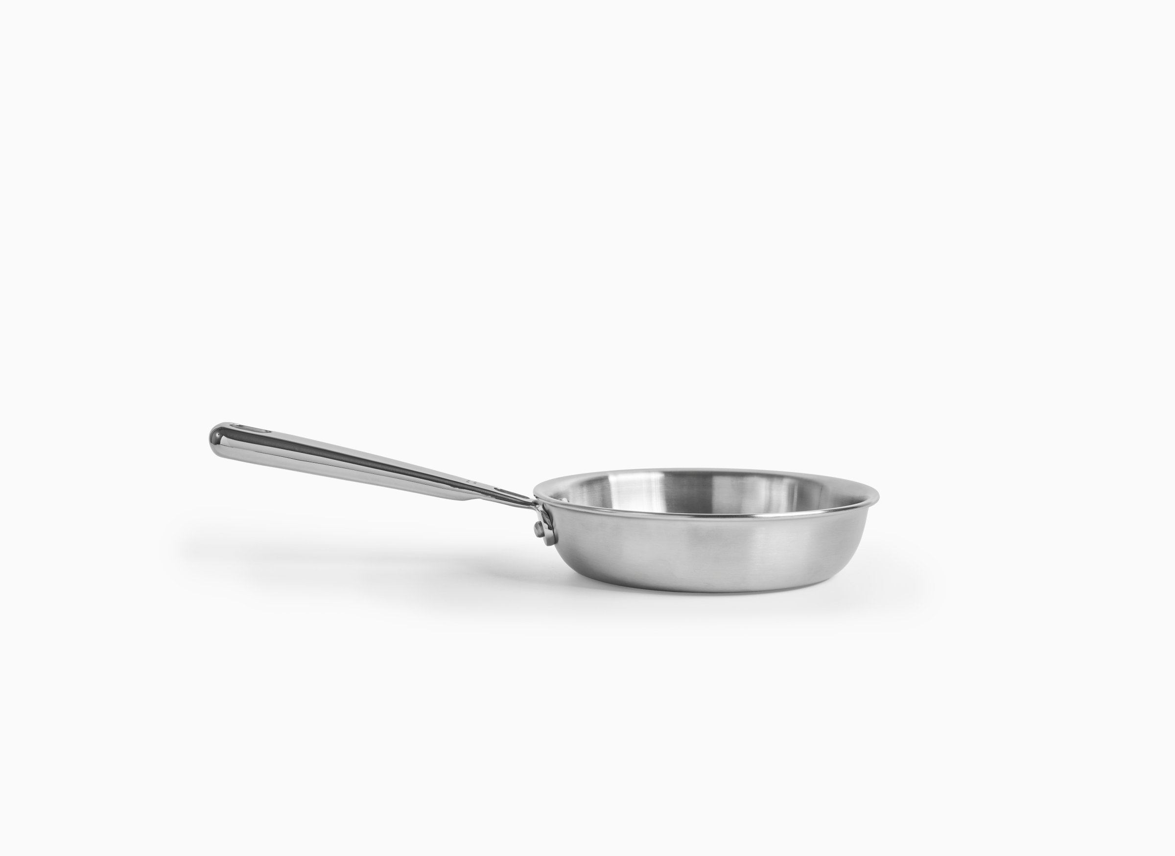 A Misen six-inch stainless steel skillet with a long handle is shown from a slightly elevated side angle. The skillet is empty and has a polished, reflective surface. The background is solid white.