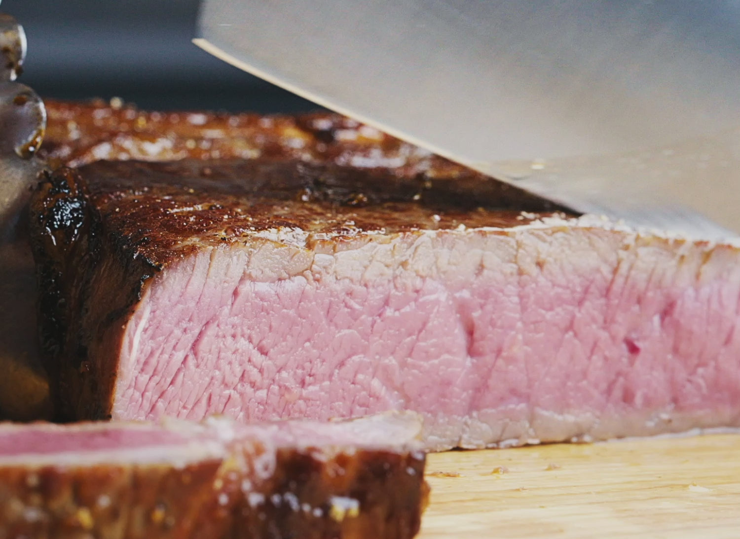 A Misen 6.5 inch Chef's Knife in blue slicing through a medium steak, held by a pair of stainless steel tongs.